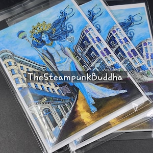 Op de afbeelding: Een stapel kunstafdrukken in doorzichtige plastic hoezen. Elke afdruk toont een blauwhuidige figuur met blauw haar, een kroon en een staf, tegen een stadsgezicht. De tekst "TheSteampunkBuddha" is zichtbaar op de afdrukken.