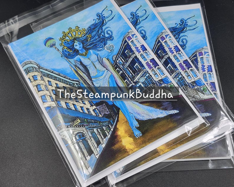 Op de afbeelding: Een stapel kunstafdrukken in doorzichtige plastic hoezen. Elke afdruk toont een blauwhuidige figuur met blauw haar, een kroon en een staf, tegen een stadsgezicht. De tekst "TheSteampunkBuddha" is zichtbaar op de afdrukken.