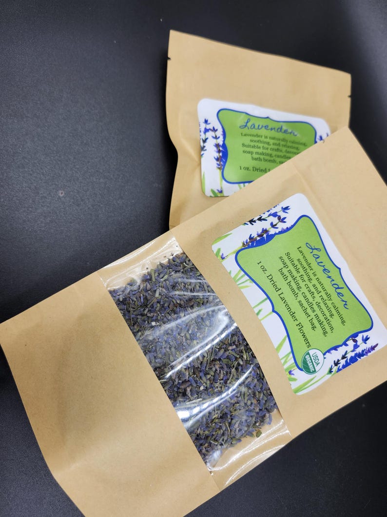 以下が含まれることがあります： 透明な窓が付いた2つの茶色の紙袋。乾燥ラベンダーの花が詰まっています。各バッグには「ラベンダー」と書かれたラベルがあり、石鹸作りやキャンドル作りなどの用途が記載されています。バッグには乾燥ラベンダーの花が28グラム入っています。