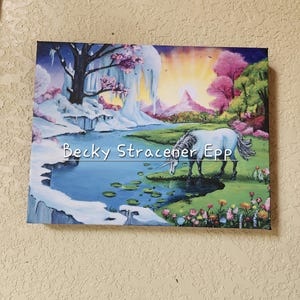 Puede incluir: Una pintura sobre lienzo que representa un paisaje sereno con un unicornio bebiendo de un estanque. La obra presenta una escena invernal con nieve, hielo y una colorida puesta de sol. El texto en la pintura dice "Becky Stracener Epp".