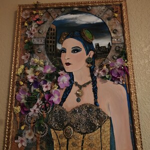 May include: A framed mixed-media artwork featuring a portrait of a person with blue braided hair, goggles, and a corset adorned with metallic gears. The piece is decorated with artificial purple and white flowers, small bee figures, and a gold frame.