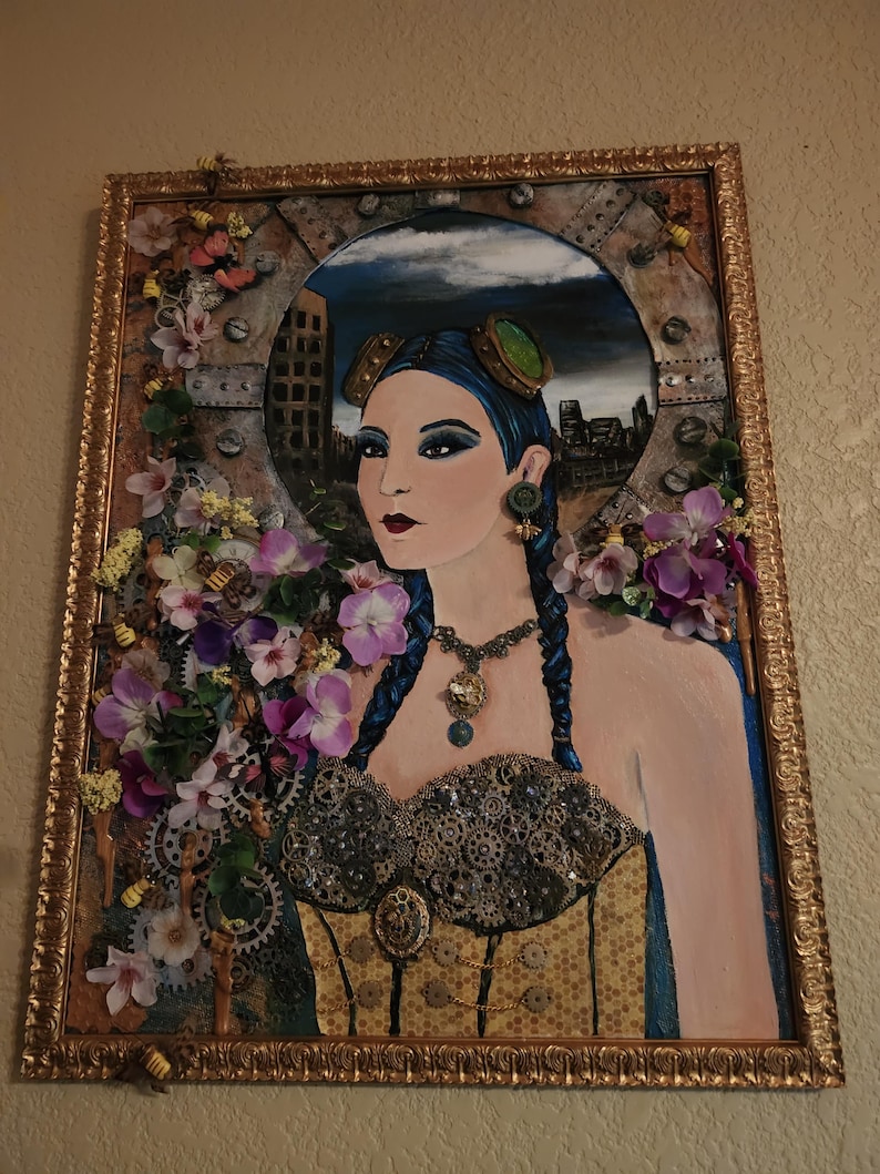 May include: A framed mixed-media artwork featuring a portrait of a person with blue braided hair, goggles, and a corset adorned with metallic gears. The piece is decorated with artificial purple and white flowers, small bee figures, and a gold frame.