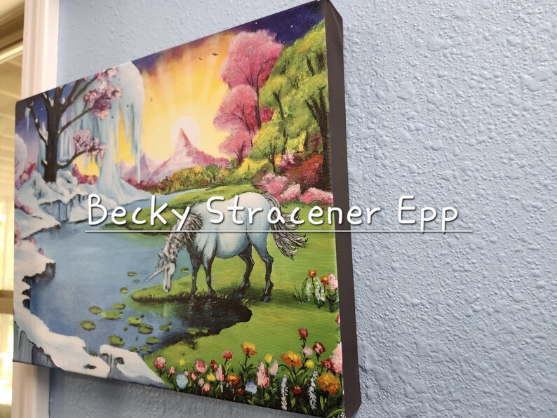 Puede incluir: Una impresi&oacute;n art&iacute;stica en lienzo que representa un unicornio bebiendo de un estanque en un paisaje de fantas&iacute;a. La obra de arte incluye una cascada, flores coloridas y el texto "Becky Stracener Epp". El fondo presenta una puesta de sol y &aacute;rboles rosas.