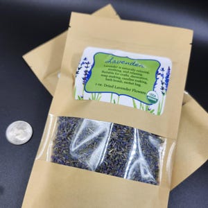 以下が含まれることがあります： 乾燥ラベンダーの花が入った、透明な窓付きの茶色の紙袋。袋のラベルには「ラベンダー」と書かれており、用途が記載されています。ラベルには「1 oz. Dried Lavender Flowers」とも書かれています。