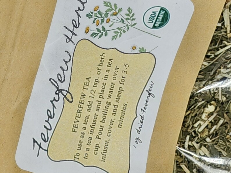 Puede incluir: Un paquete de t&eacute; de matricaria seca. La etiqueta incluye el texto "Feverfew Tea" e instrucciones de uso. La etiqueta tambi&eacute;n presenta un dibujo de una planta y el sello USDA Organic.