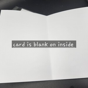 Op de afbeelding: Een open, blanco wenskaart met een witte binnenkant. De tekst "card is blank on inside" wordt weergegeven op een grijs rechthoekig label. De kaart ligt op een donkere ondergrond.