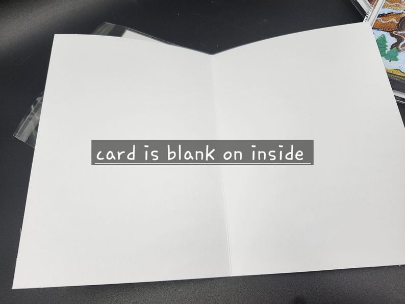 Op de afbeelding: Een open, blanco wenskaart met een witte binnenkant. De tekst "card is blank on inside" wordt weergegeven op een grijs rechthoekig label. De kaart ligt op een donkere ondergrond.