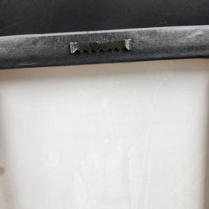 Puede incluir: Primer plano de la parte posterior de una impresi&oacute;n en lienzo enmarcada. El marco negro tiene un colgador de dientes de sierra para montaje en pared. El lienzo es blanco con un sutil patr&oacute;n floral.