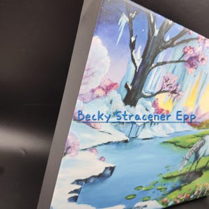 Puede incluir: Una obra de arte en lienzo que presenta una pintura de paisaje con un r&iacute;o, monta&ntilde;as y &aacute;rboles con flores rosas. La obra de arte tiene una paleta de colores azul, blanco y amarillo. El nombre del artista, "Becky Stracener Epp", es visible en el lienzo.