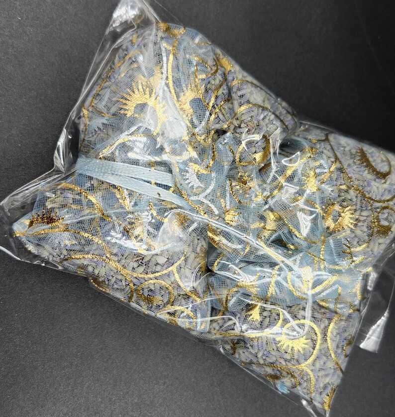 Puede incluir: Una bolsa de pl&aacute;stico transparente que contiene varias bolsas de tela de malla azul y dorada. Las bolsas est&aacute;n decoradas con patrones florales dorados y atadas con una cinta azul claro. La est&eacute;tica general es delicada y ornamentada.