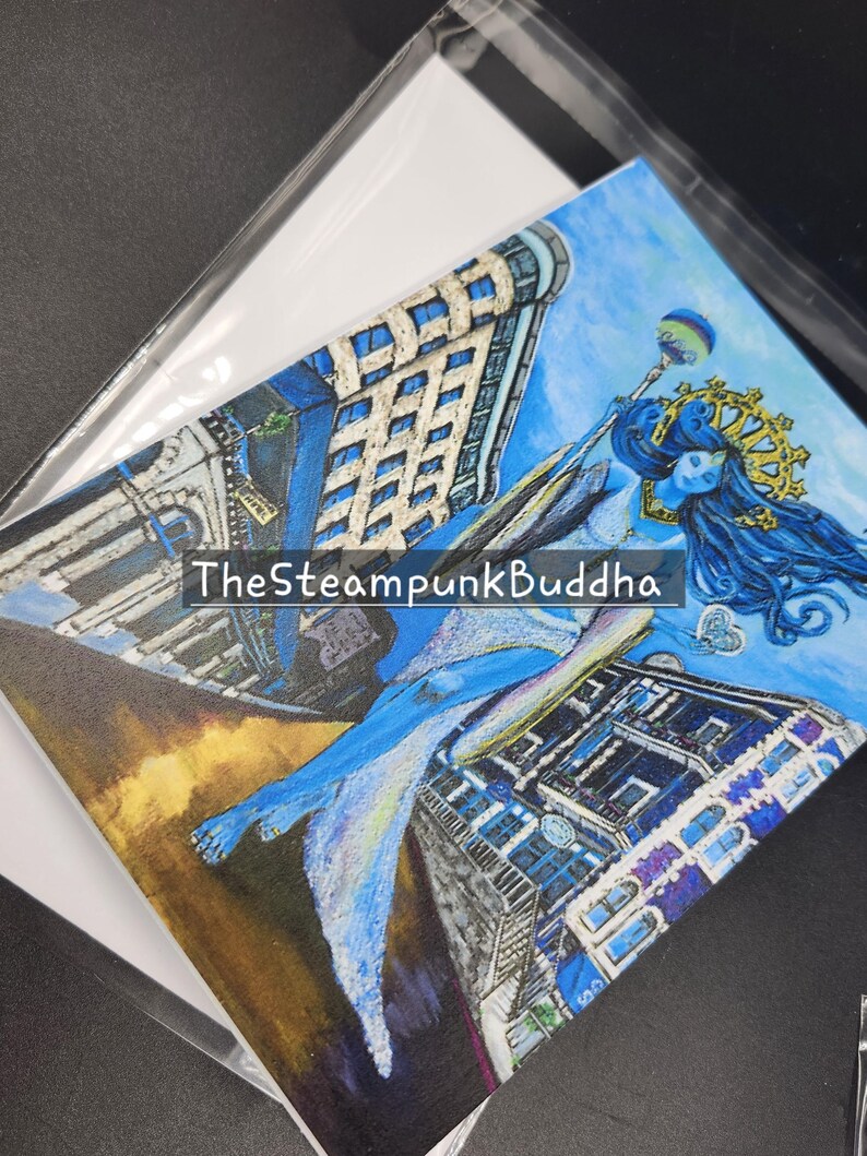 Op de afbeelding: Een originele kunstafdruk met een blauwhuidige figuur met lang blauw haar, een gouden kroon en een staf, tegen een achtergrond van gestileerde gebouwen. De tekst "TheSteampunkBuddha" is zichtbaar. Het kunstwerk zit in een transparante plastic hoes.