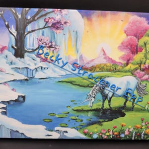 Puede incluir: Una pintura sobre lienzo representa un paisaje sereno con un unicornio blanco bebiendo de un estanque azul. La escena incluye acantilados cubiertos de nieve, &aacute;rboles rosados ​​en flor y una vibrante puesta de sol. El texto "Becky Stracener ERP" est&aacute; en la imagen.
