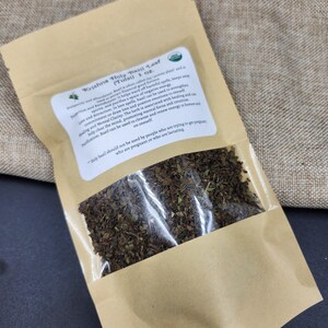 May include: A brown paper bag with a clear window, filled with dried green leaves. The bag has a label with text that reads "Krishna Holy Basil Leaf (Tulsi) 1 oz."