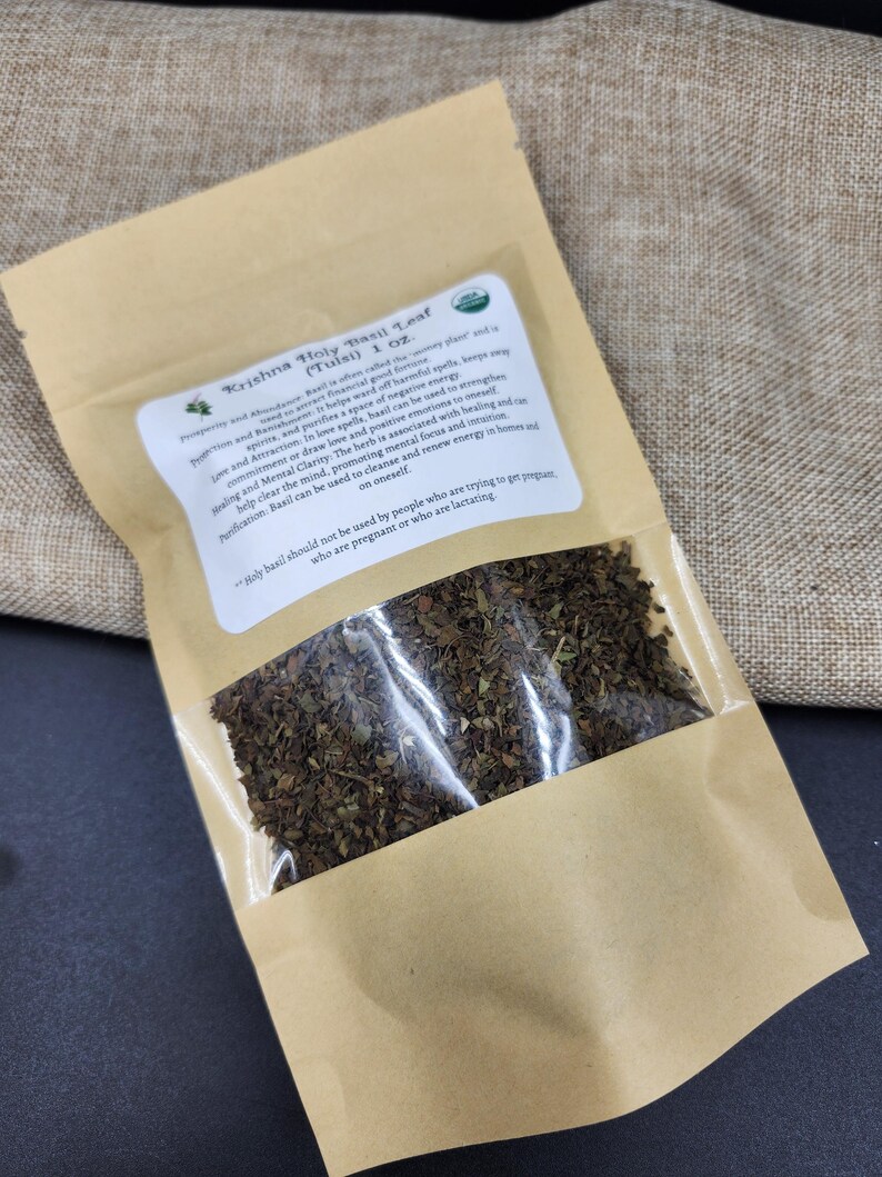 May include: A brown paper bag with a clear window, filled with dried green leaves. The bag has a label with text that reads "Krishna Holy Basil Leaf (Tulsi) 1 oz."