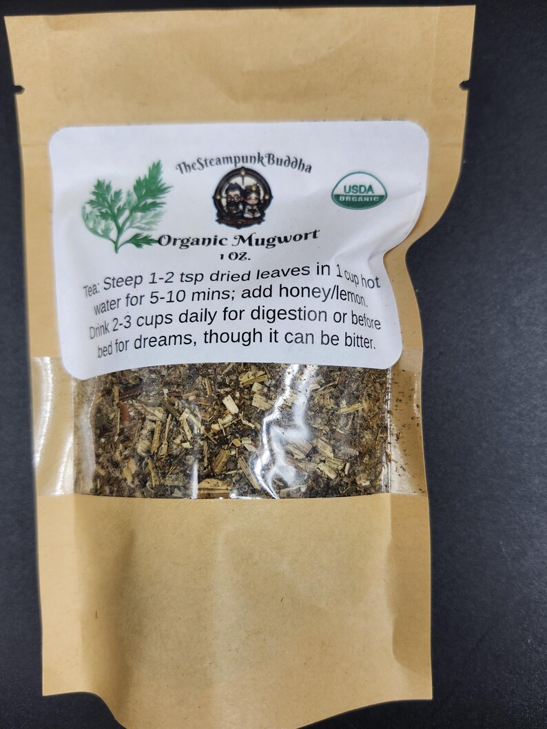 May include: A brown paper bag with a clear window displaying dried herbs. The label reads "Organic Mugwort" with instructions for tea preparation. The Steampunk Buddha logo and USDA Organic seal are also visible.