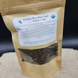 May include: A brown paper bag of Krishna Holy Basil Leaf (Tulsi) with a USDA Organic label. The bag contains dried basil leaves and has a white label with text describing the herb's uses and warnings. The bag is 1 oz.