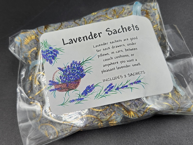 Puede incluir: Una bolsa de pl&aacute;stico transparente que contiene dos saquitos de lavanda. Los saquitos est&aacute;n decorados con un estampado floral dorado y azul. Una etiqueta blanca muestra el texto "Saquitos de lavanda" y una descripci&oacute;n del producto, con un dibujo de lavanda.