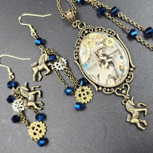 May include: A steampunk-style jewelry set featuring a necklace and earrings. The necklace has an oval pendant with a vintage image, gears, and blue accents. The earrings and necklace have bronze-colored chains, unicorn charms, and blue beads.