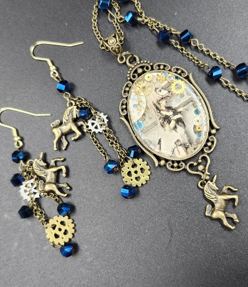 May include: A steampunk-style jewelry set featuring a necklace and earrings. The necklace has an oval pendant with a vintage image, gears, and blue accents. The earrings and necklace have bronze-colored chains, unicorn charms, and blue beads.