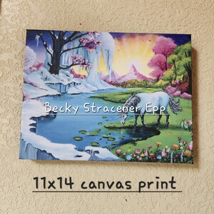 Puede incluir: Impresi&oacute;n en lienzo de 28x36 cm que representa un paisaje de fantas&iacute;a con un unicornio blanco bebiendo de un estanque. La obra de arte incluye una zona nevada, &aacute;rboles rosas y una puesta de sol. El nombre del artista, Becky Stracener Epp, es visible.