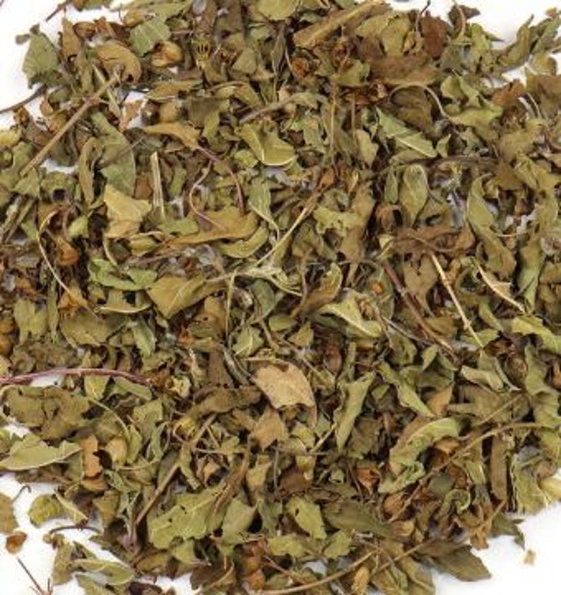 May include: Close-up of dried, loose leaf herbs with a mix of green, brown, and tan colors. The leaves and stems are scattered across a white surface, showing various textures and shapes. The image highlights the natural, organic appearance of the herbs.
