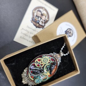 Peut inclure: Pendentif ovale avec un design steampunk, comprenant des engrenages, un oiseau et d'autres &eacute;l&eacute;ments dans une bo&icirc;te. Le pendentif a un cadre argent&eacute; avec des d&eacute;tails de roses et une cha&icirc;ne. La bo&icirc;te a un int&eacute;rieur en velours noir.
