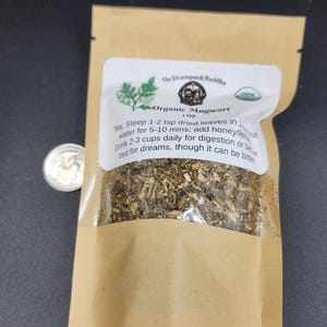 May include: A brown paper bag with a clear window containing dried herbs. The bag has a white label with the text "Organic Mugwort" and instructions for use. A US quarter is next to the bag.