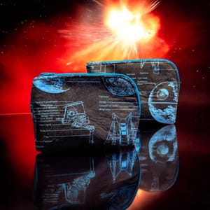 May include: Two black zippered pouches with blue trim. One pouch features a blueprint of a spaceship with the text "Top View, Canopy, Forward Fuel Tanks, Wing Tanks". The other pouch features a blueprint of the Death Star with the text "Superstructure, Service View, Interior,  Superlaser,  Escape Pod Bay".