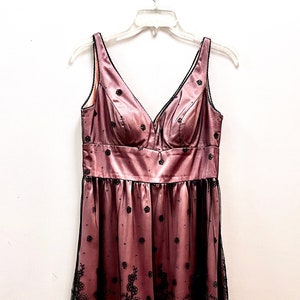 May include: A pink satin dress with black lace overlay and a V-neckline. The dress has a fitted bodice and a flowing skirt.