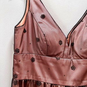 May include: A sleeveless, blush pink tulle dress with black floral embroidery. The dress has a V-neckline and a fitted bodice.