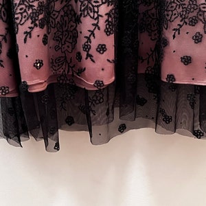 May include: A pink skirt with black floral embroidery and a black tulle underskirt.