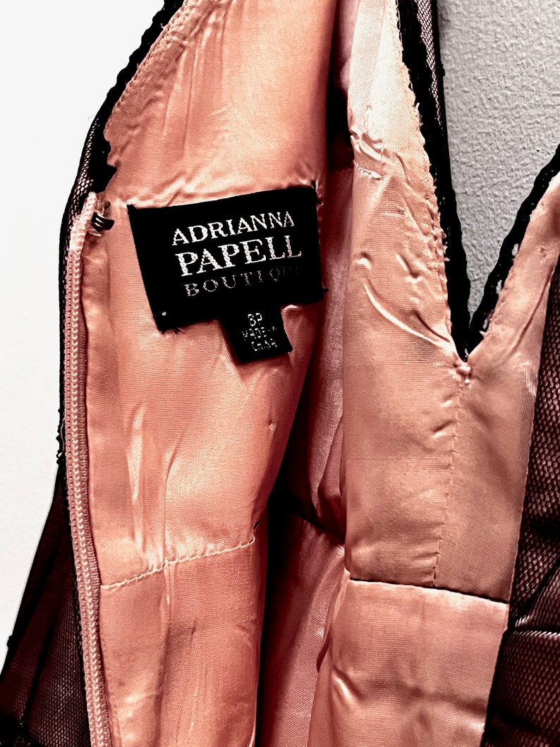 May include: A black and pink dress with a black lace trim. The dress has a label that reads "Adrianna Papell Boutique" and "Size 8 Made in China".