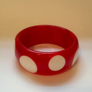 Może przedstawiać: Czerwona plastikowa bransoletka z białymi kropkami.
