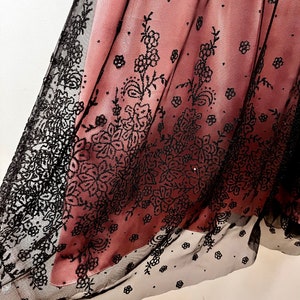 May include: A pink and black tulle fabric with a floral pattern. The fabric is sheer and has a delicate, feminine look.