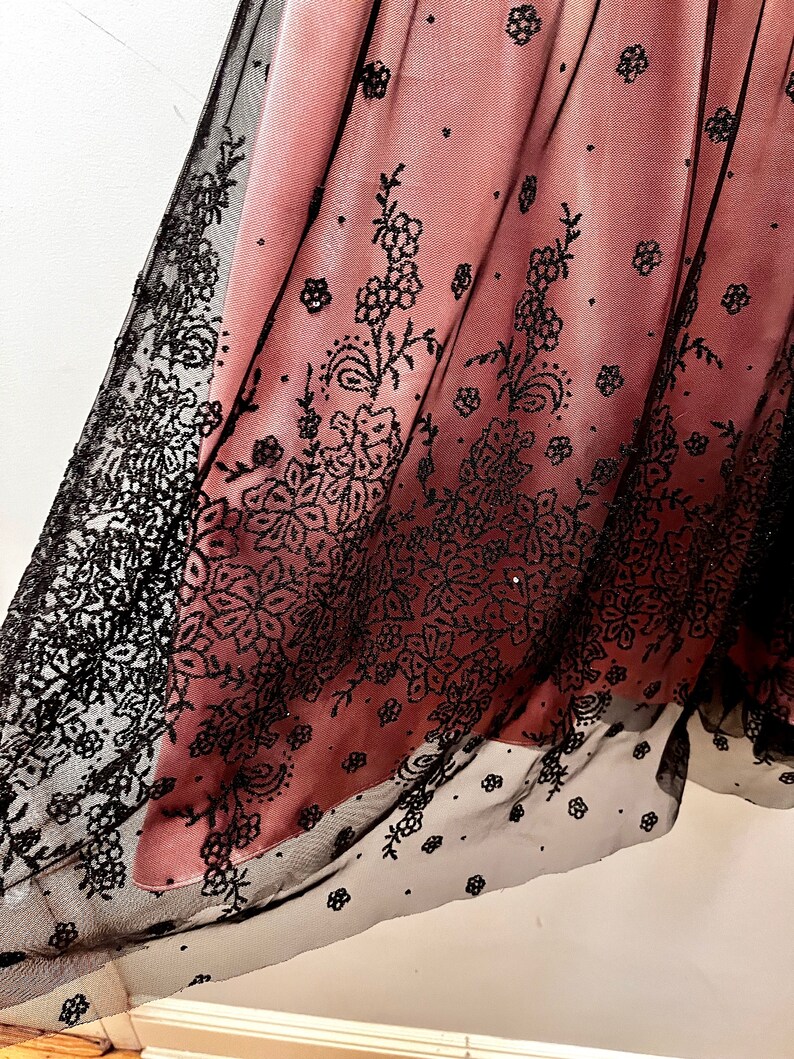 May include: A pink and black tulle fabric with a floral pattern. The fabric is sheer and has a delicate, feminine look.