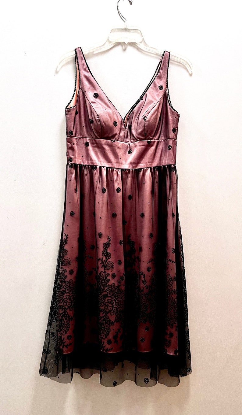 May include: A pink satin dress with black lace overlay and a V-neckline. The dress has a fitted bodice and a flowing skirt.