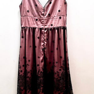 May include: A sleeveless, pink satin dress with black floral embroidery and a black tulle overlay. The dress has a V-neckline and a back zipper closure.