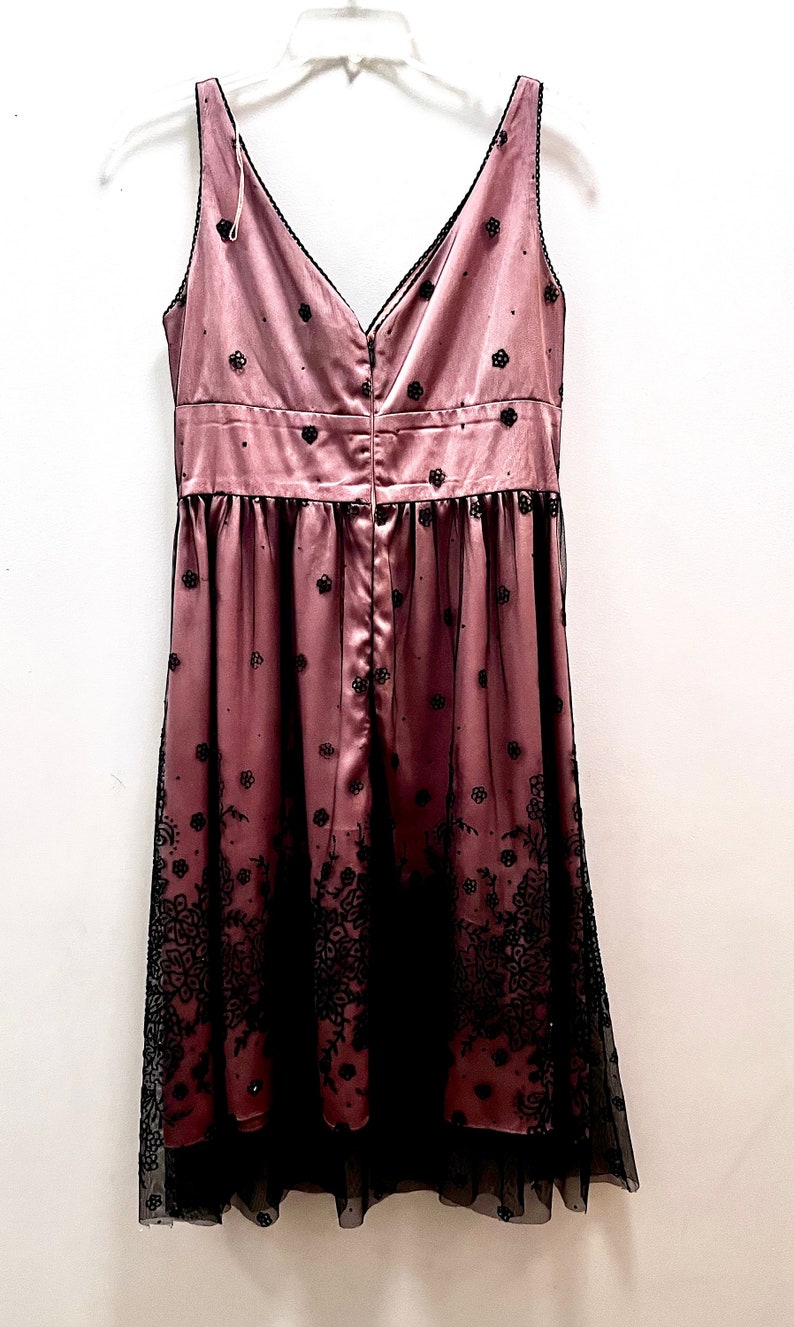 May include: A sleeveless, pink satin dress with black floral embroidery and a black tulle overlay. The dress has a V-neckline and a back zipper closure.