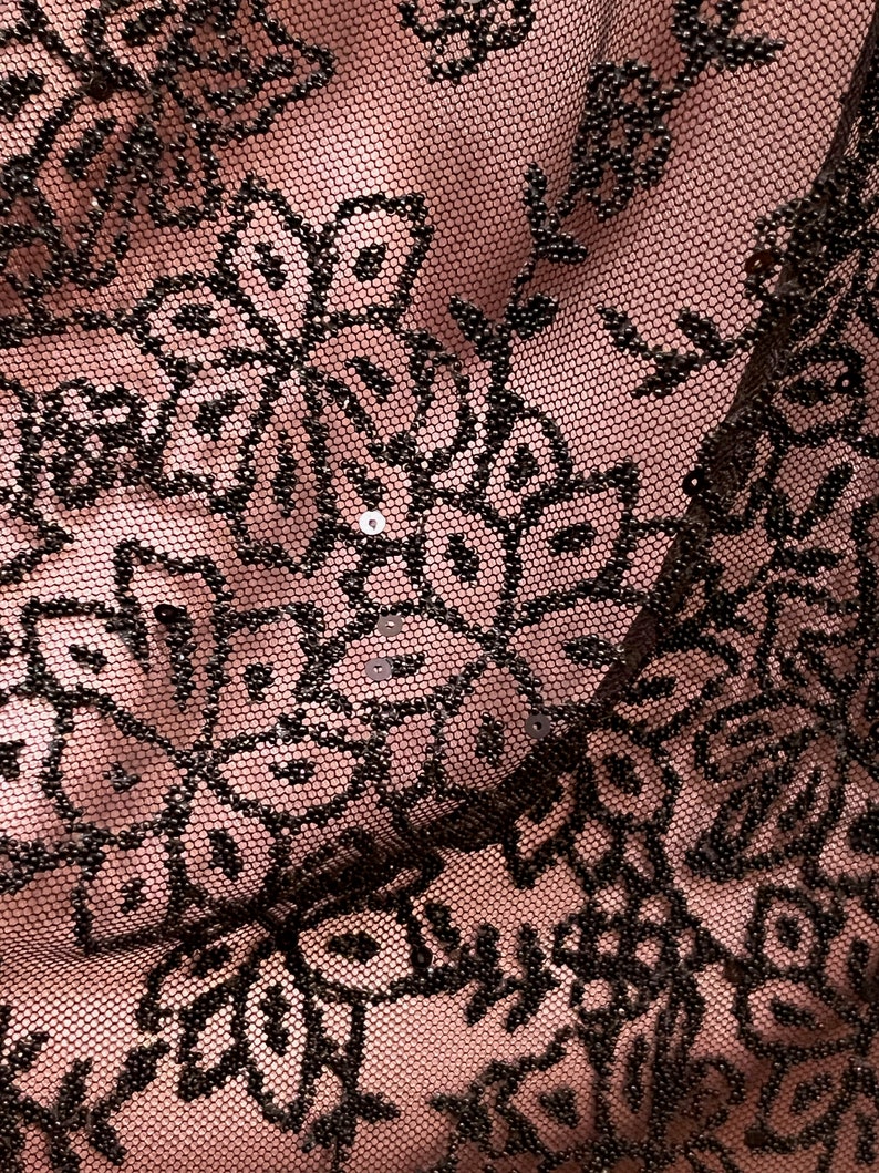 May include: Close-up of black lace fabric with a floral pattern and small sequins. The fabric is sheer and has a delicate texture.