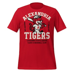 Op de afbeelding: Rood t-shirt met een cartoon tijger met een honkbalpet en een knuppel. Het shirt toont de tekst "ALEXANDRIA TIGERS" met "ESTD 1920" en "LOUISIANA STATE LEAGUE CLASS D BASEBALL CLUB".