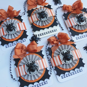 May include: Four black and orange Halloween gift tags with a spider and web design. Each tag has the word "EEEEEEEK!" printed on it.