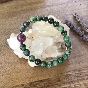 May include: A green and pink gemstone bracelet with silver beads. The bracelet is made of round beads and is strung on a stretchy cord.