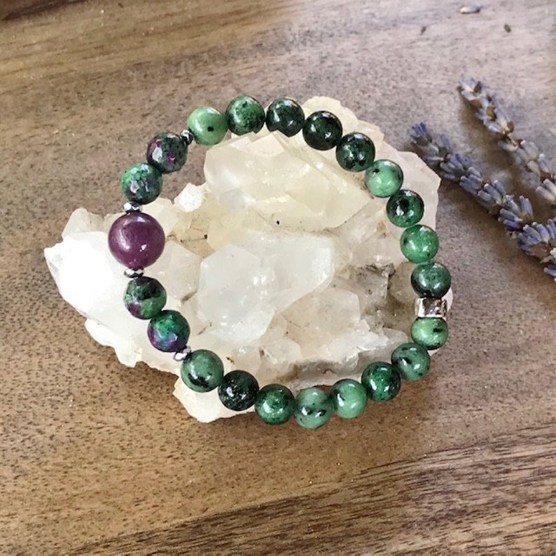 May include: A green and pink gemstone bracelet with silver beads. The bracelet is made of round beads and is strung on a stretchy cord.