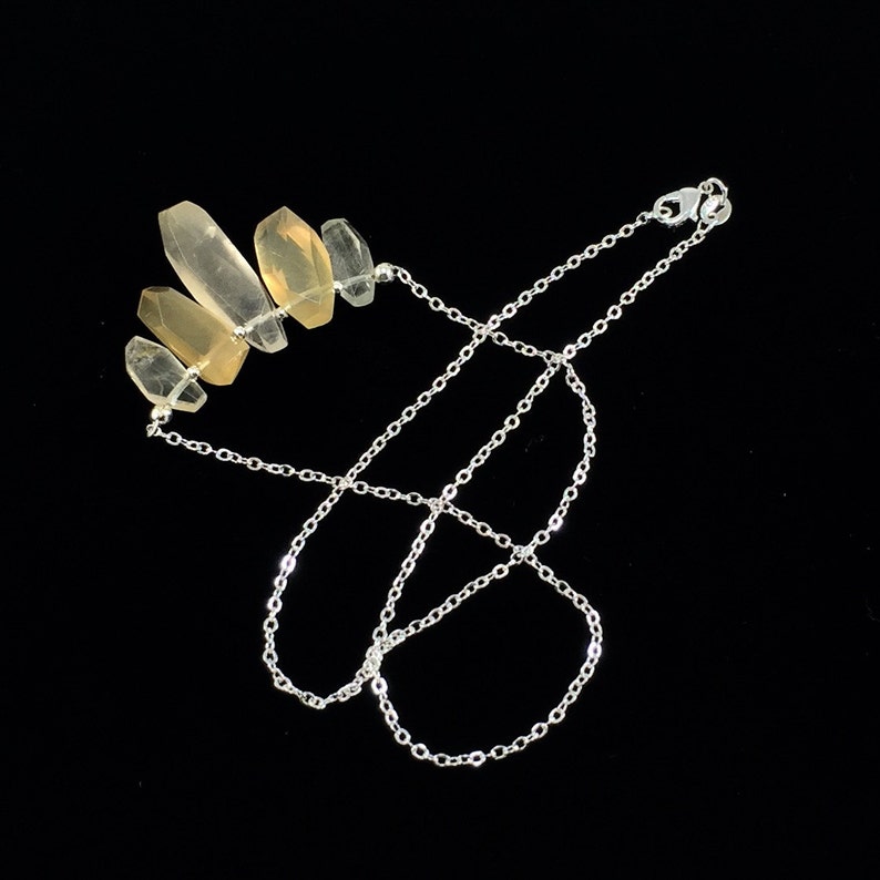 May include: A silver chain necklace with a cluster of five light yellow crystal points.