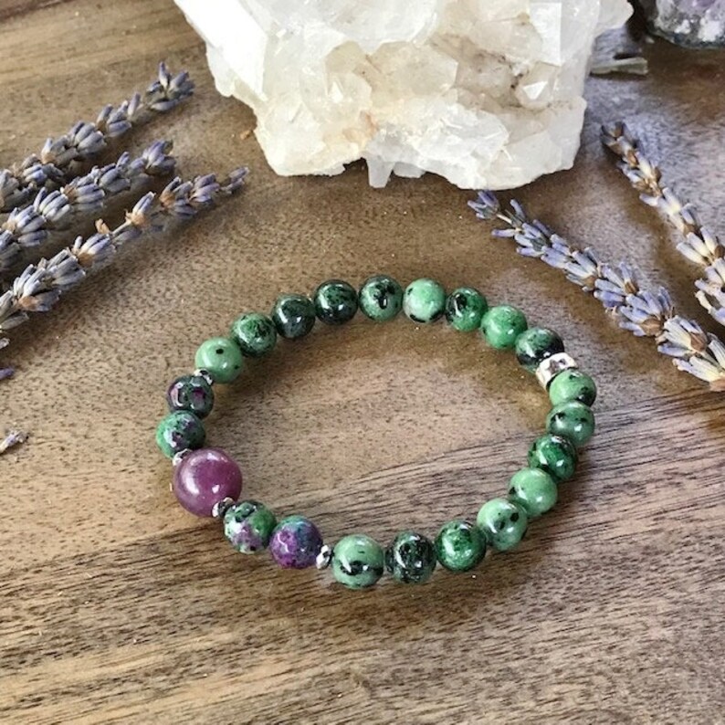 May include: A green and pink gemstone bracelet with silver beads. The bracelet is made of round beads and is strung on a stretchy cord.