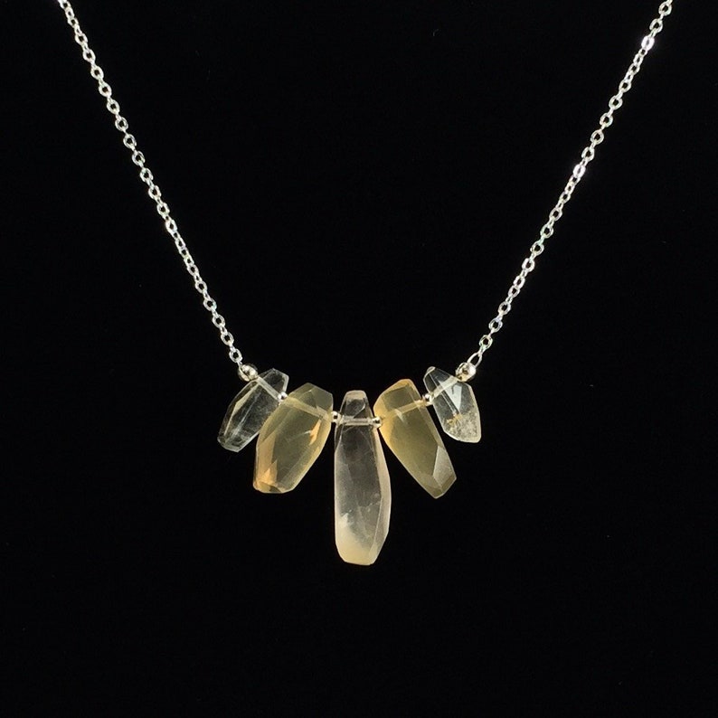 May include: A silver chain necklace with five clear and light brown crystal pendants. The crystals are faceted and have a natural, irregular shape.