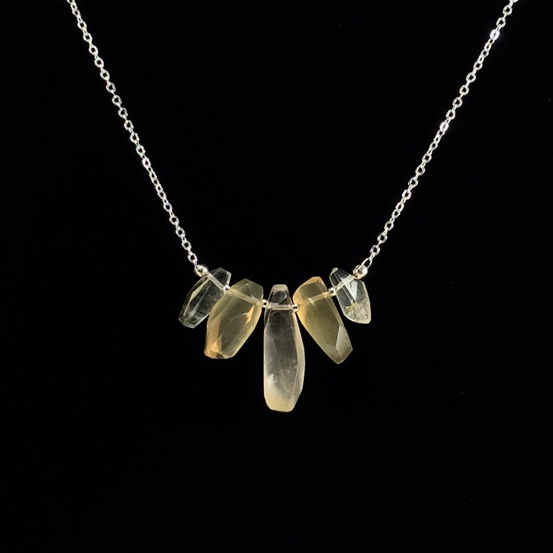 May include: A silver chain necklace with five light brown, faceted, teardrop-shaped stones hanging from it.