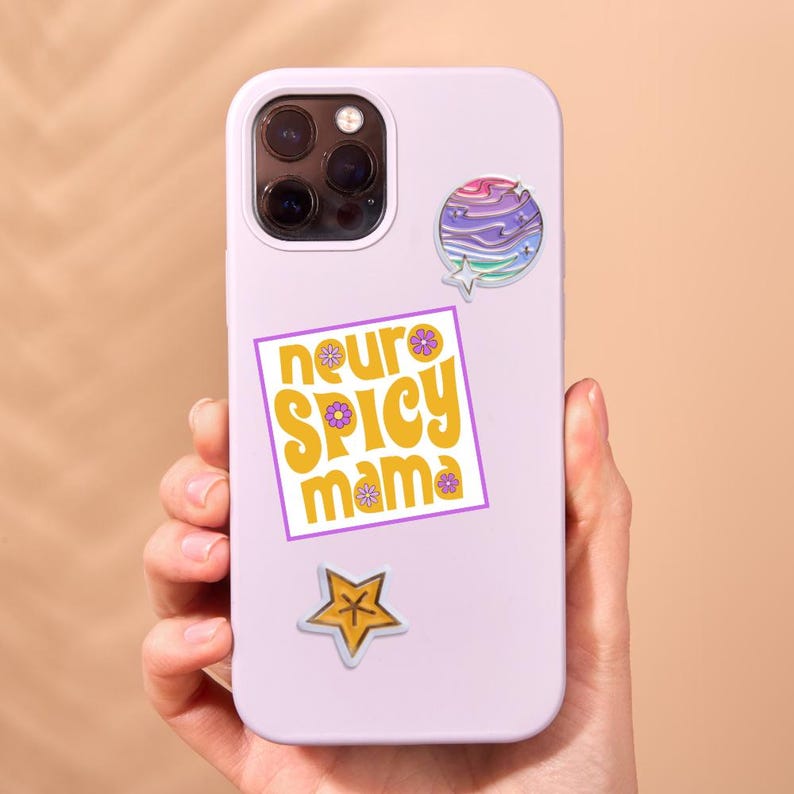 May include: A light purple phone case with multiple stickers. The stickers include a colorful planet design, a star, and a square sticker with the words "neuro spicy mama" in yellow and purple.