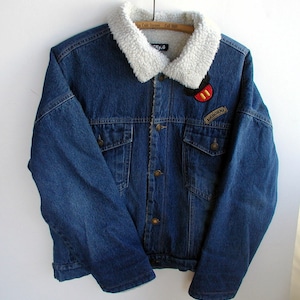 May include: A blue denim jacket with a white faux fur collar and a Mickey Mouse patch on the left chest. The jacket also has a patch that says "Airborne".