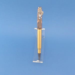 May include: A gold and brown pen with a deer head design on the top. The pen is on a clear acrylic stand.